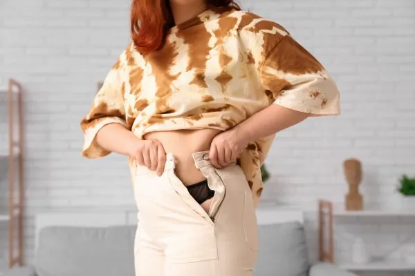 Image of woman trying to do her trousers up after pregnancy weight gain Herne