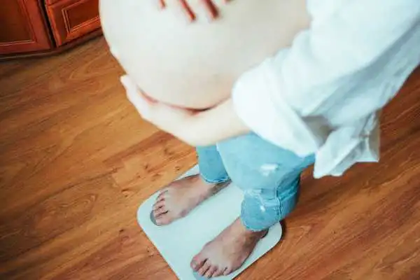 Image of woman weighing herself and experiencing weight gain through pregnancy Herne